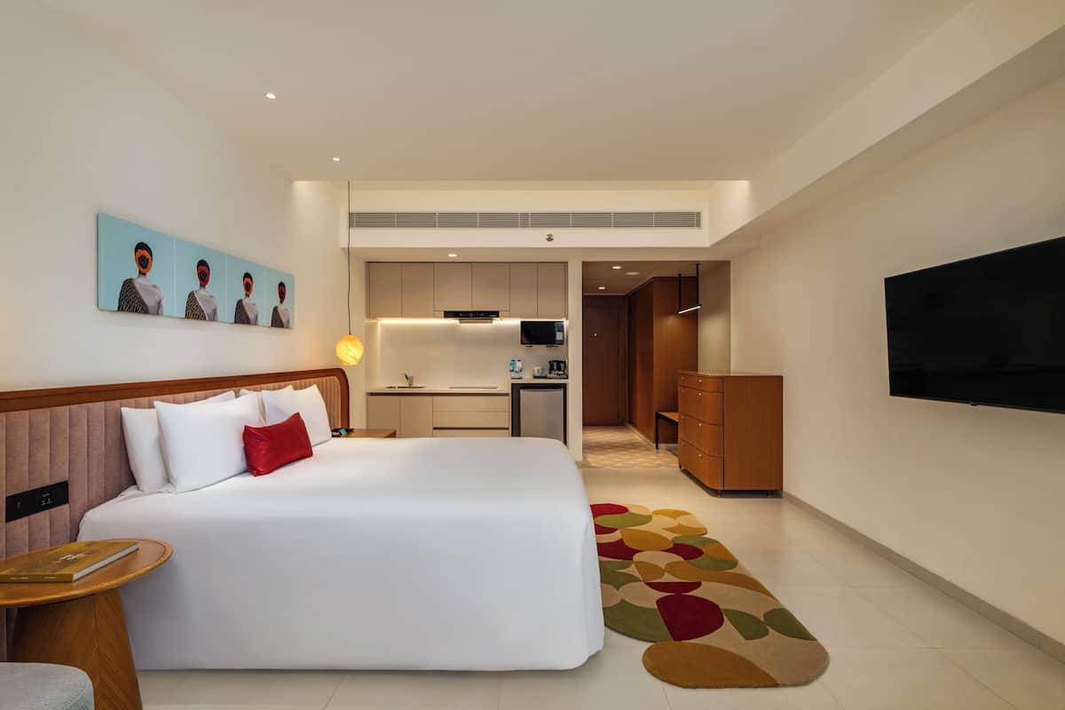 Habitación de hotel con una cama grande, un escritorio, una kitchenette, un televisor y una alfombra estampada.