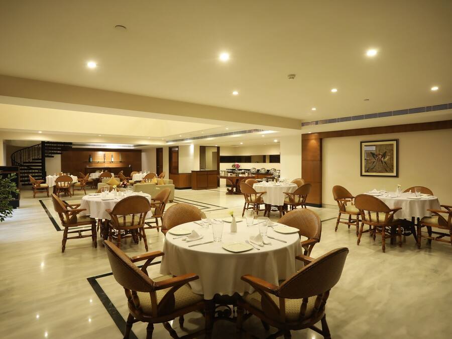 A spacious dining area with round tables and chairs, a staircase in the background, and a kitchen area visible through an open door.