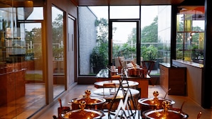 A modern dining area with large windows, a view of greenery, and a series of tables with golden decorative elements. - Greenpark Chennai (Chennai)