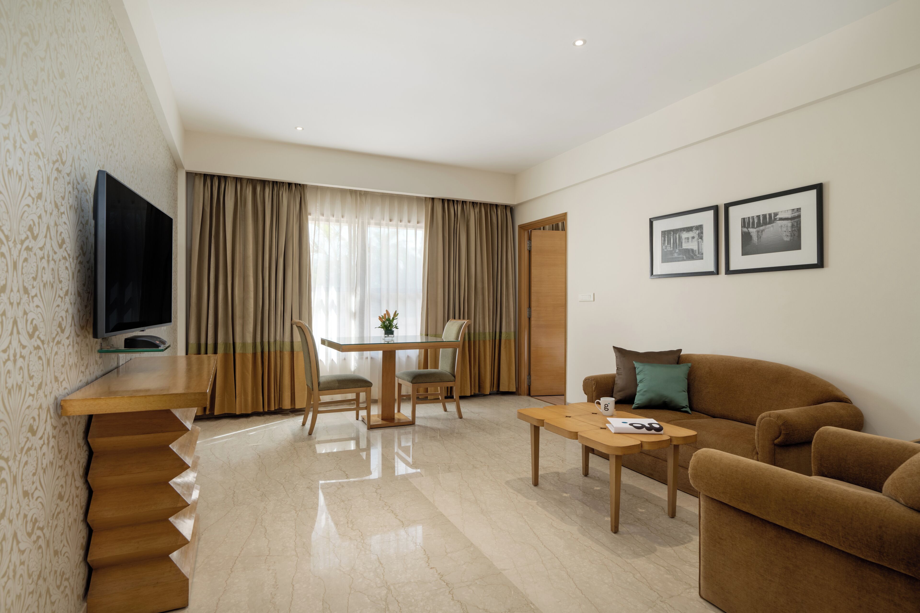 A modern living room with a flat-screen TV, a wooden dining table with chairs, a sofa, and a coffee table.
