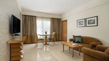 A modern living room with a flat-screen TV, a wooden dining table with chairs, a sofa, and a coffee table.
