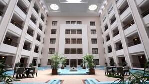 Un vestíbulo de hotel de varios pisos con piscina central, múltiples balcones y plantas de interior.