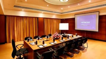 A conference room with a long table, chairs, a projector screen displaying "HITACHI", and a floral arrangement.