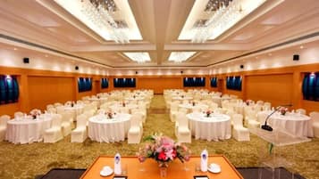 Un amplio salón de conferencias con mesas redondas y sillas blancas, un atril y una decoración floral.