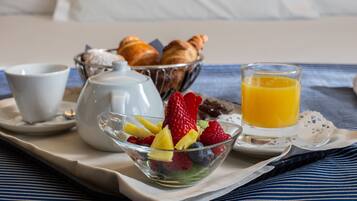 Una bandeja de desayuno con croissants, una tetera, un cuenco de fruta, una taza y un vaso de zumo de naranja.