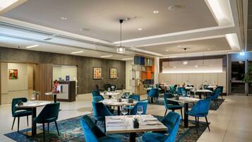 Un área de comedor moderna con sillas y mesas azules, una recepción y un ventanal grande.