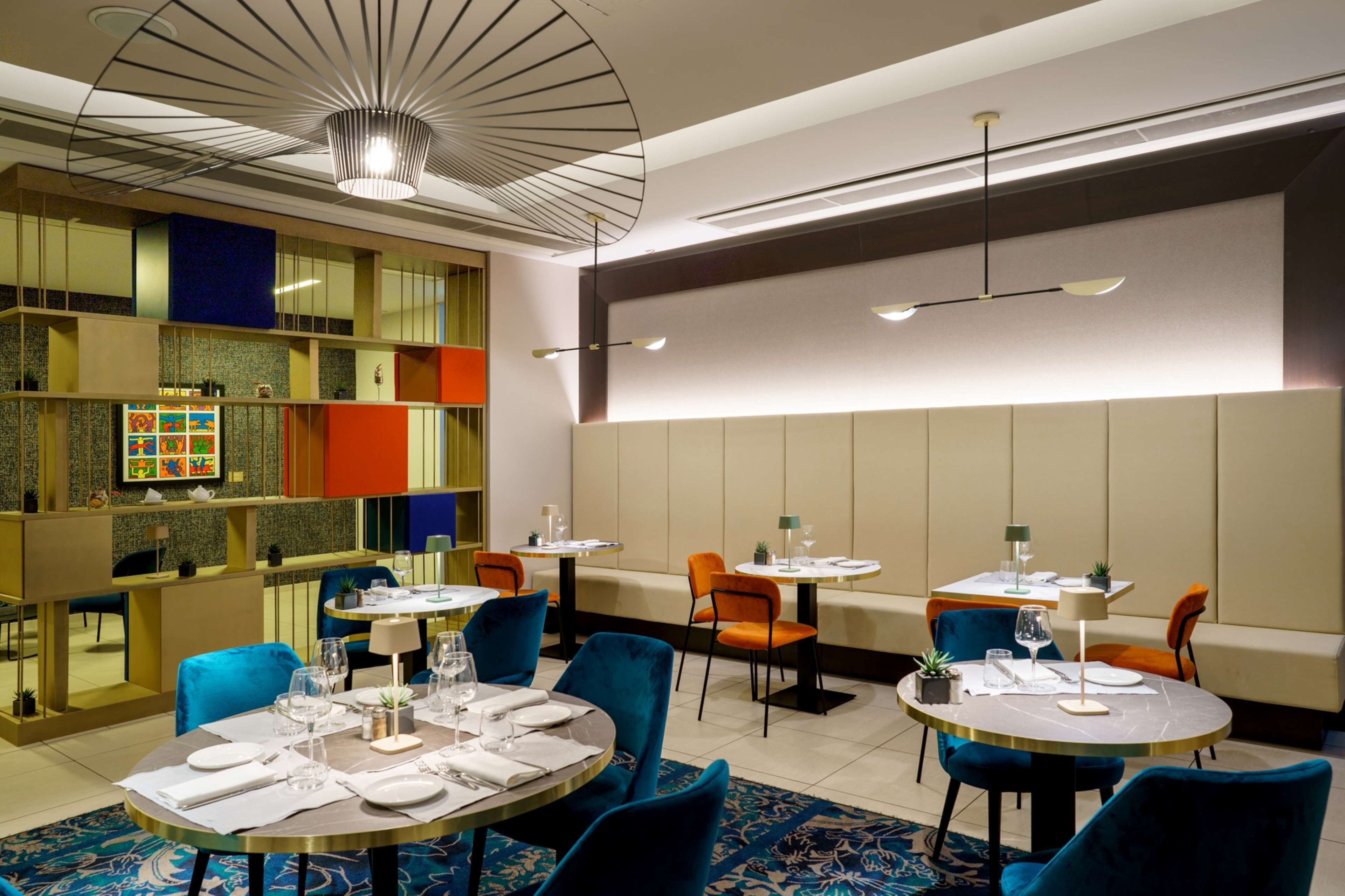 A modern restaurant with round tables, blue chairs, and a colorful wall display.