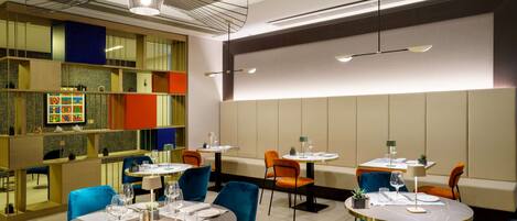 A modern restaurant with round tables, blue chairs, and a colorful wall display.