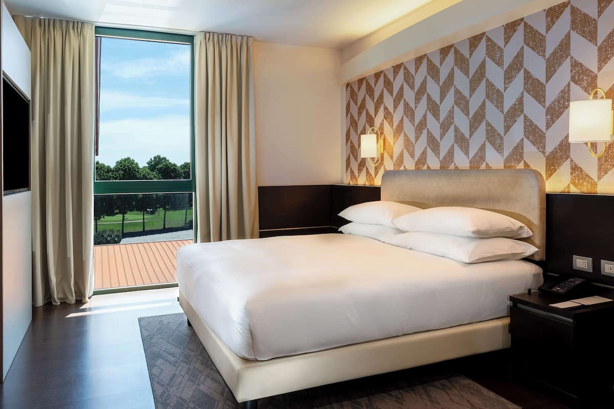 Habitación de hotel con una cama grande, vistas al exterior, pared con diseño y una mesita de noche con lámpara.