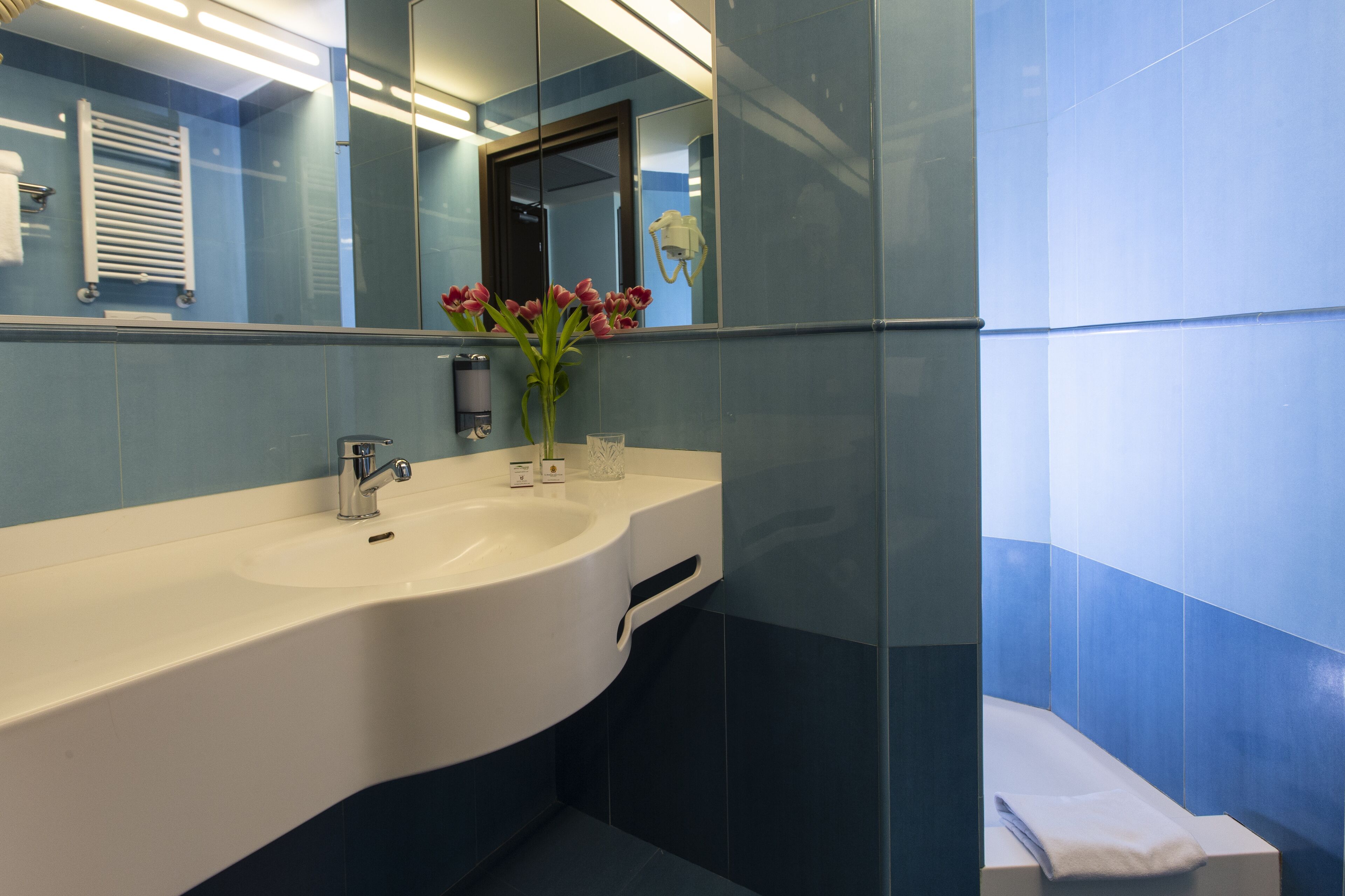 A modern bathroom with a white sink, a mirror, and a vase of flowers.