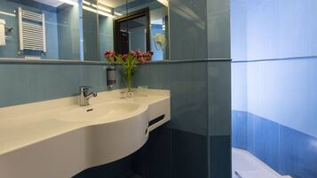A modern bathroom with a white sink, a mirror, and a vase of flowers.