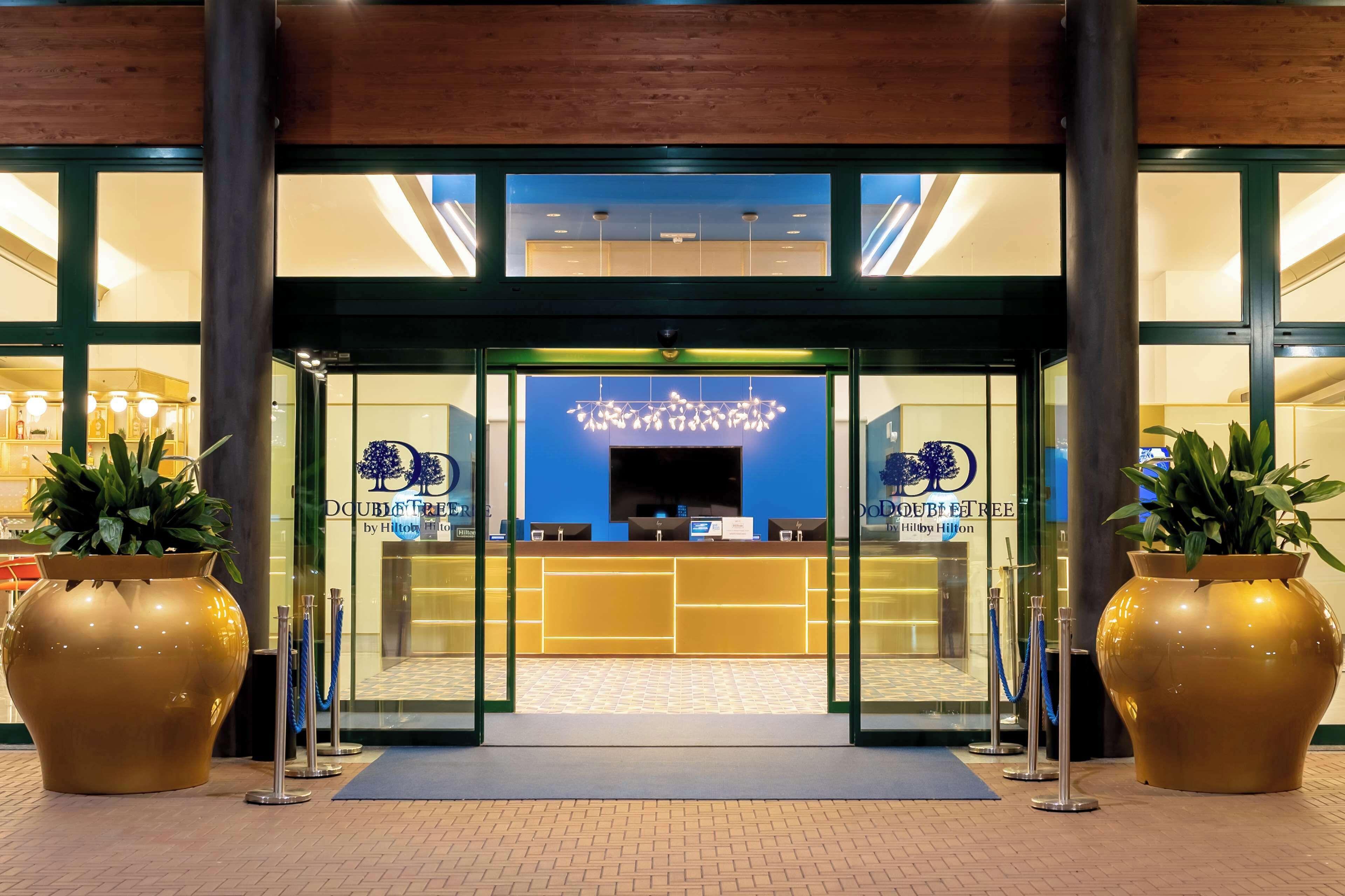 L’entrée d’un hôtel avec un comptoir d’accueil, de grands pots de plantes et un intérieur aux tons bleus.