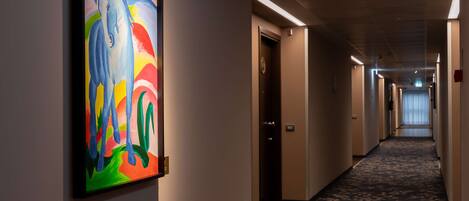 A hallway with a colorful abstract painting on the wall, a carpeted floor, and doors leading to rooms.