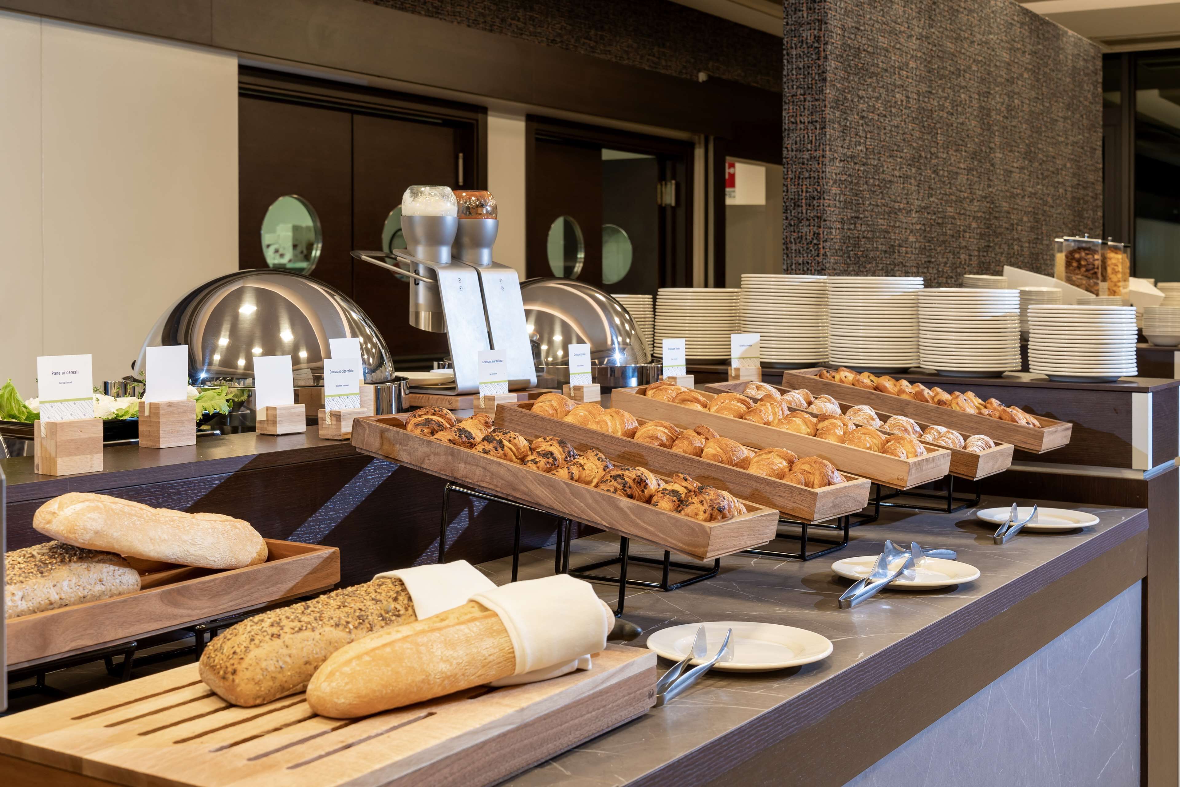 Un aparador amb diferents tipus de pa i pastissos, incloent croissants i baguettes, disposats sobre taules de fusta.