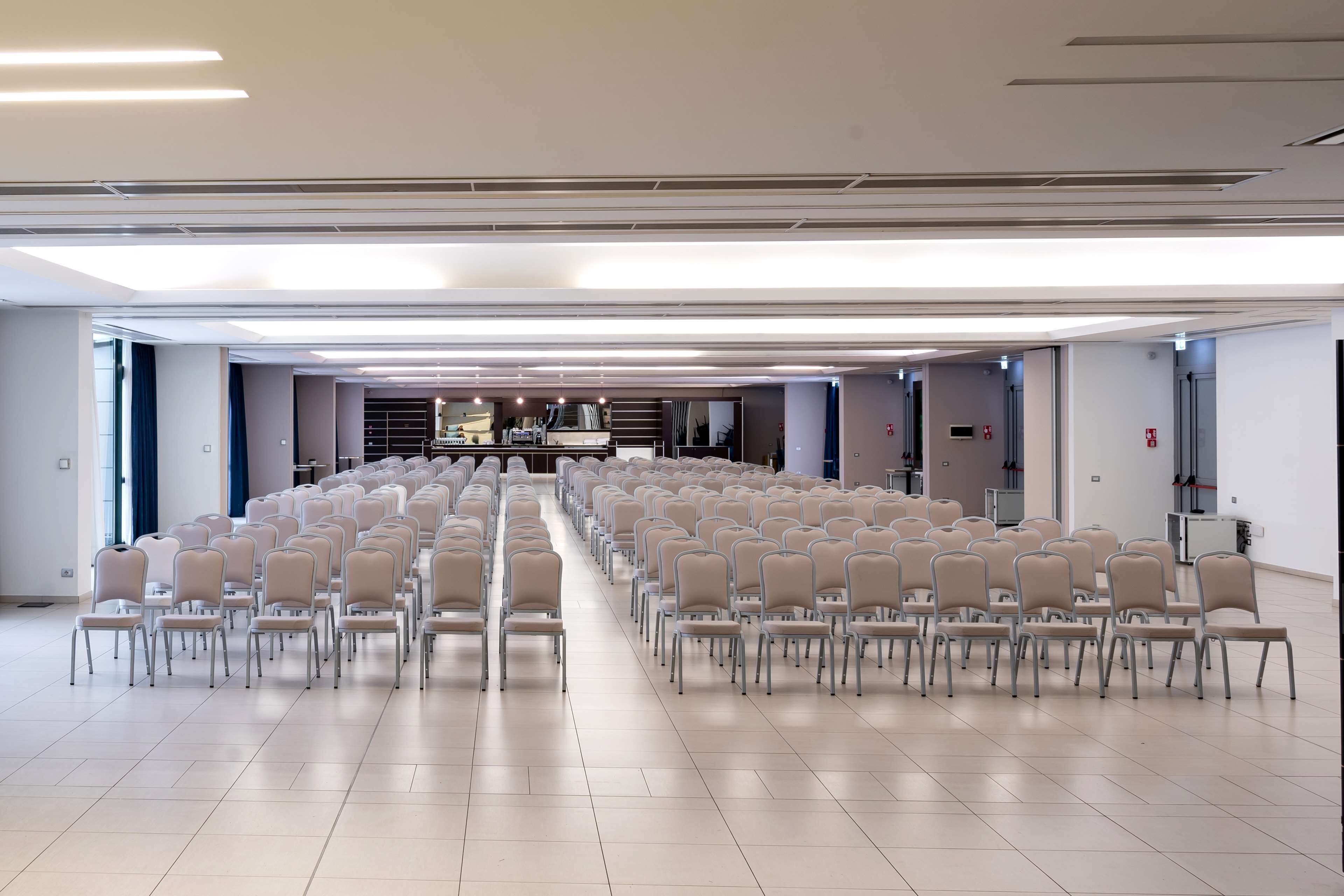 A large conference room with rows of chairs, a stage with a podium, and a modern ceiling design.