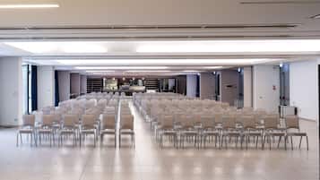 A large conference room with rows of chairs, a stage with a podium, and a modern ceiling design.