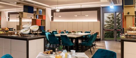A modern dining area with teal chairs, a central island with breakfast items, and a view of the outdoors.