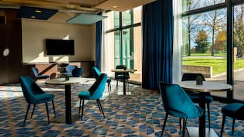 Un moderno vestíbulo de hotel con suelo de estampado geométrico, sillas tapizadas en color verde azulado y un televisor de pantalla plana montado en la pared.