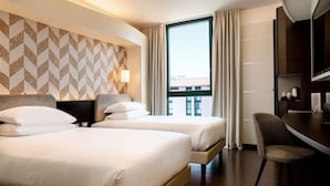 Habitación de hotel con dos camas, un escritorio, una silla, un televisor y una ventana con cortinas.