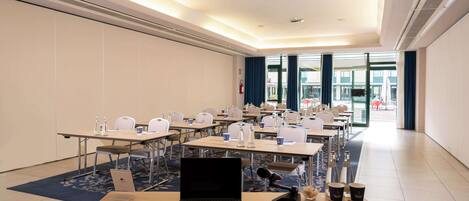 A conference room with multiple tables, chairs, and a laptop.
