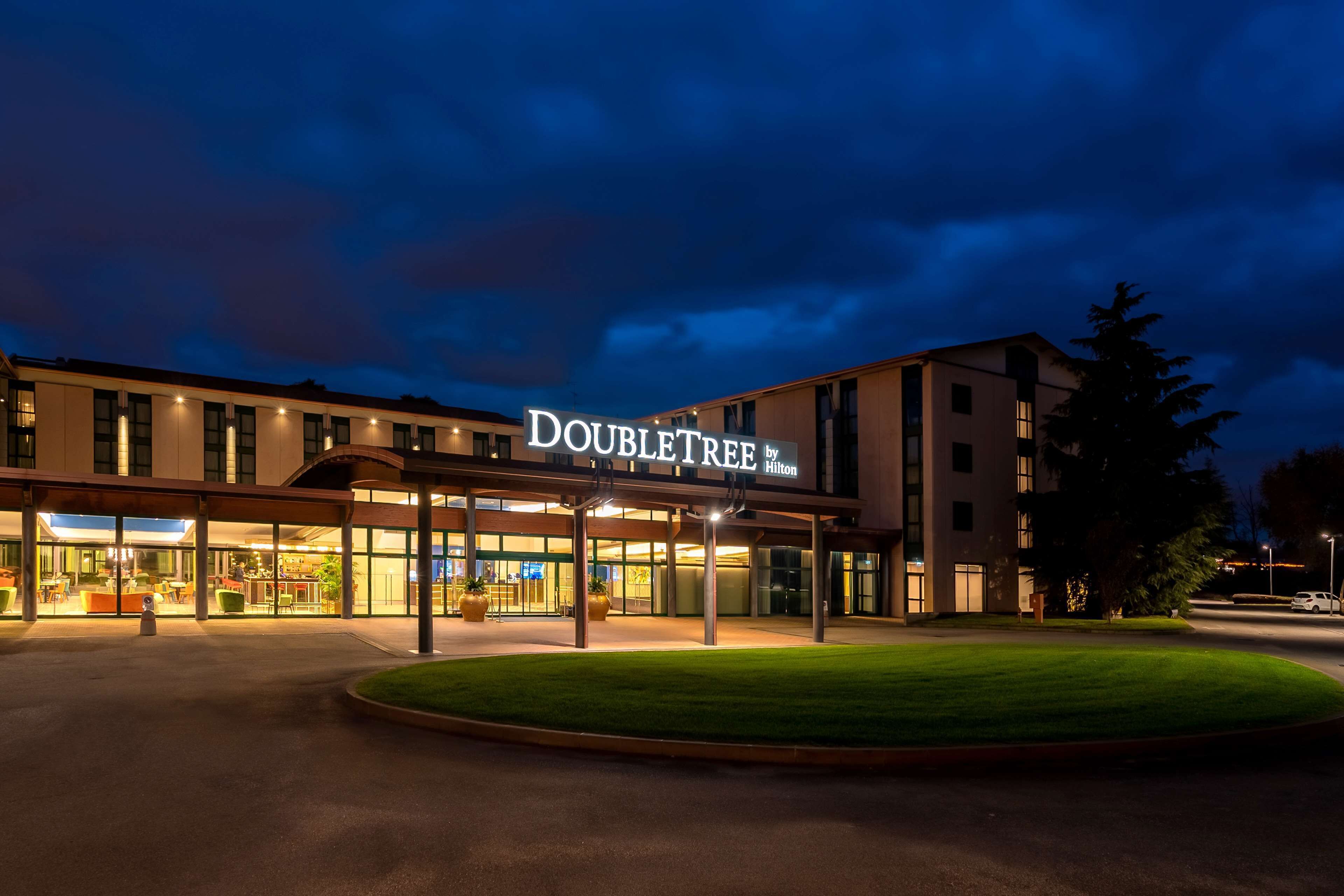 A DoubleTree by Hilton hotel at night with a well-lit entrance and a landscaped lawn.