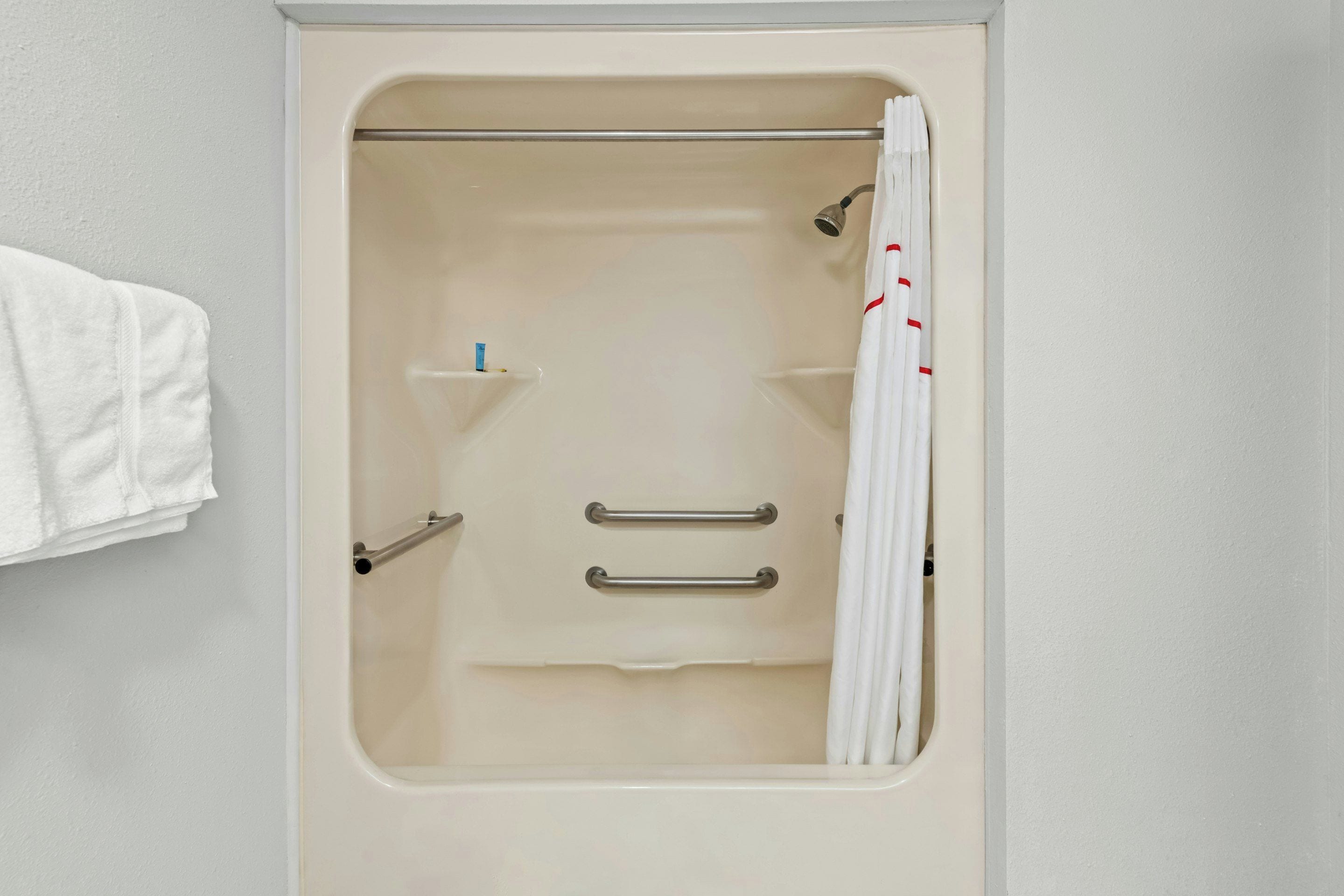 Una bañera con cortina de ducha, barras de apoyo y un perchero.