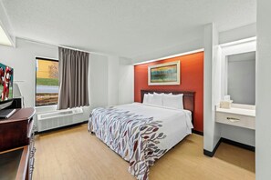 A hotel room with a bed, a desk, a TV, a window with curtains, a painting on the wall, and a bathroom mirror. - Red Roof Inn Branson (Branson)
