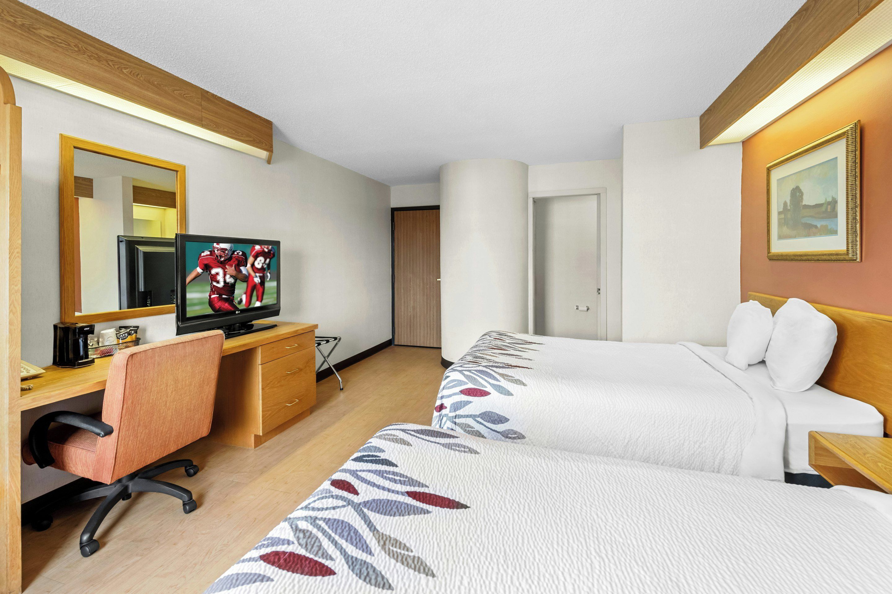 Una habitación de hotel con un escritorio de madera, televisión, dos camas y un espejo.