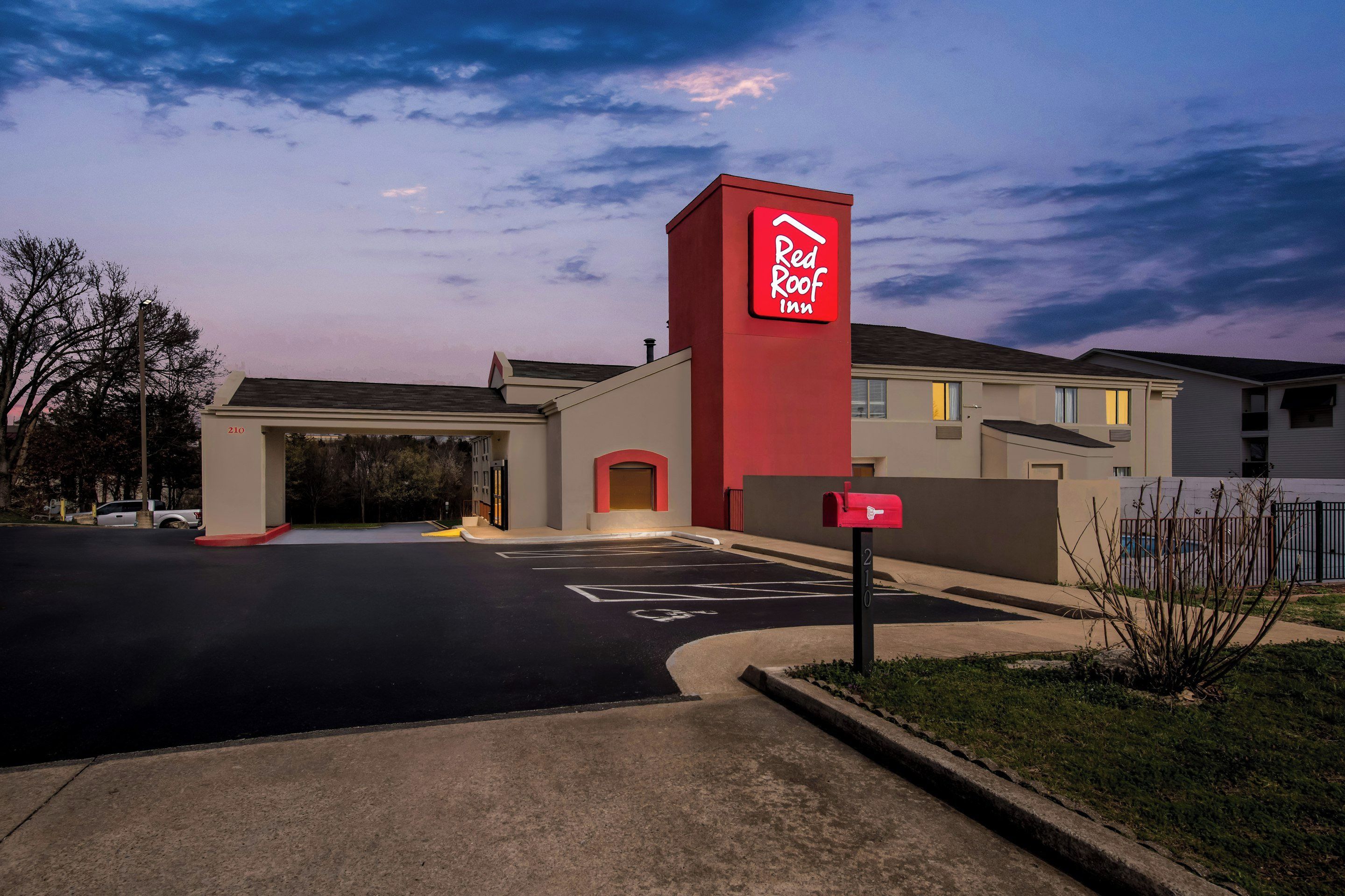 Un hotel Red Roof Inn con un edificio de color rojo y beige, un estacionamiento y un buzón.