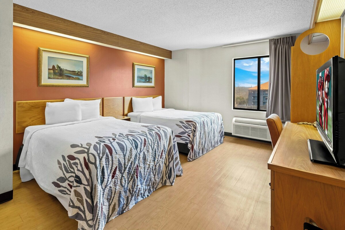 A hotel room with two beds, a desk with a TV, and a window with a view.
