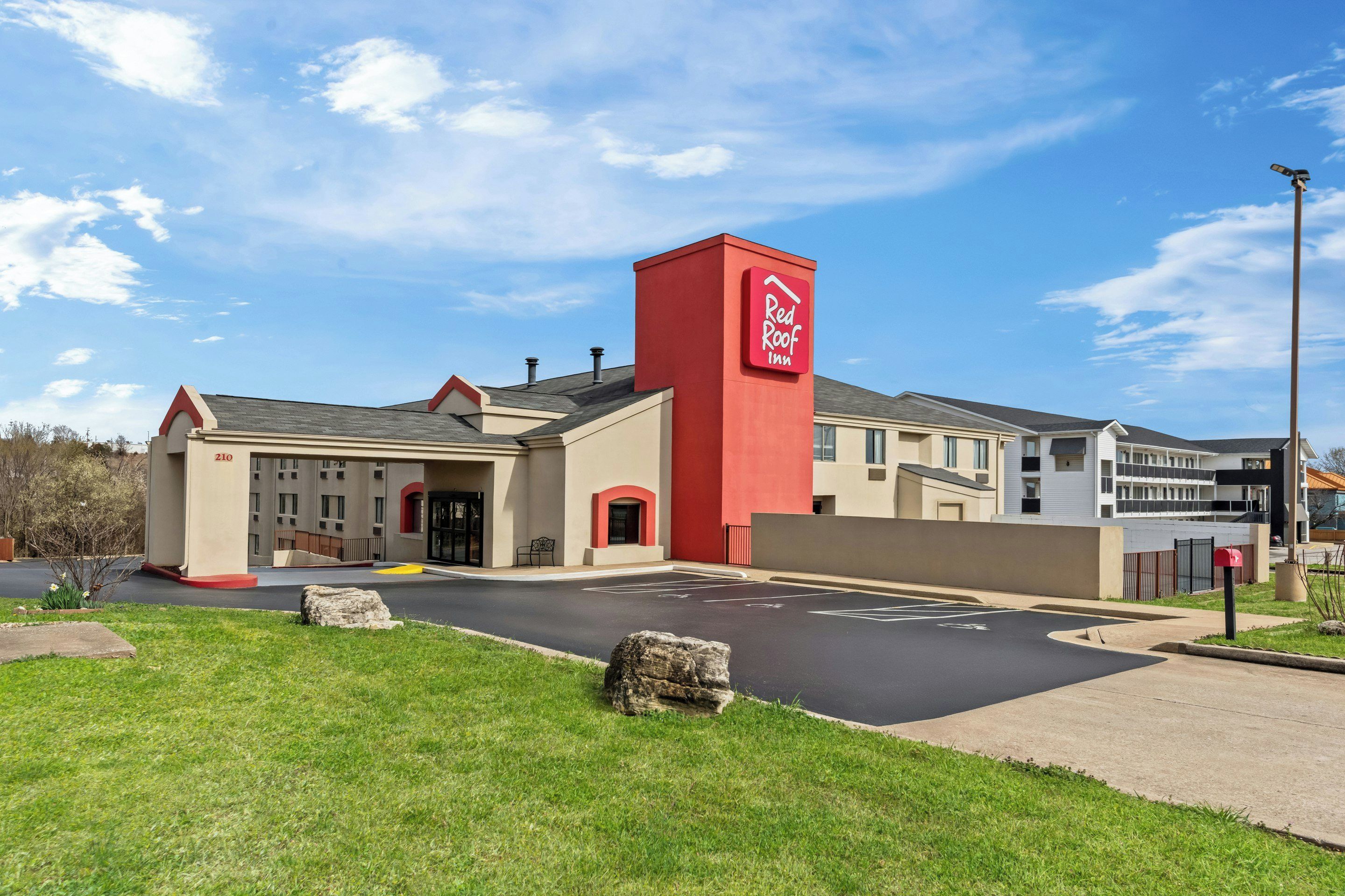 A Red Roof Inn with a red and beige facade, a parking lot, and a clear blue sky.