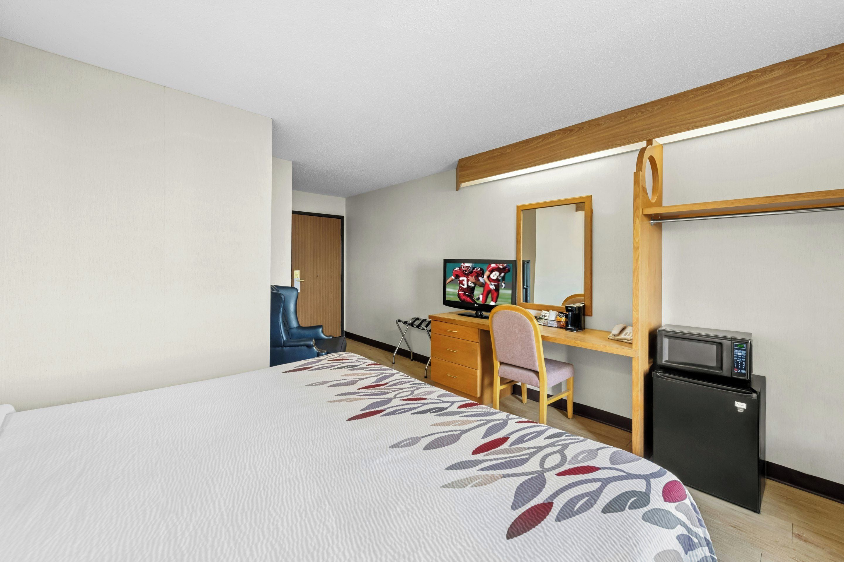 Habitación de hotel con cama, escritorio con computadora, televisión, refrigerador y espejo.