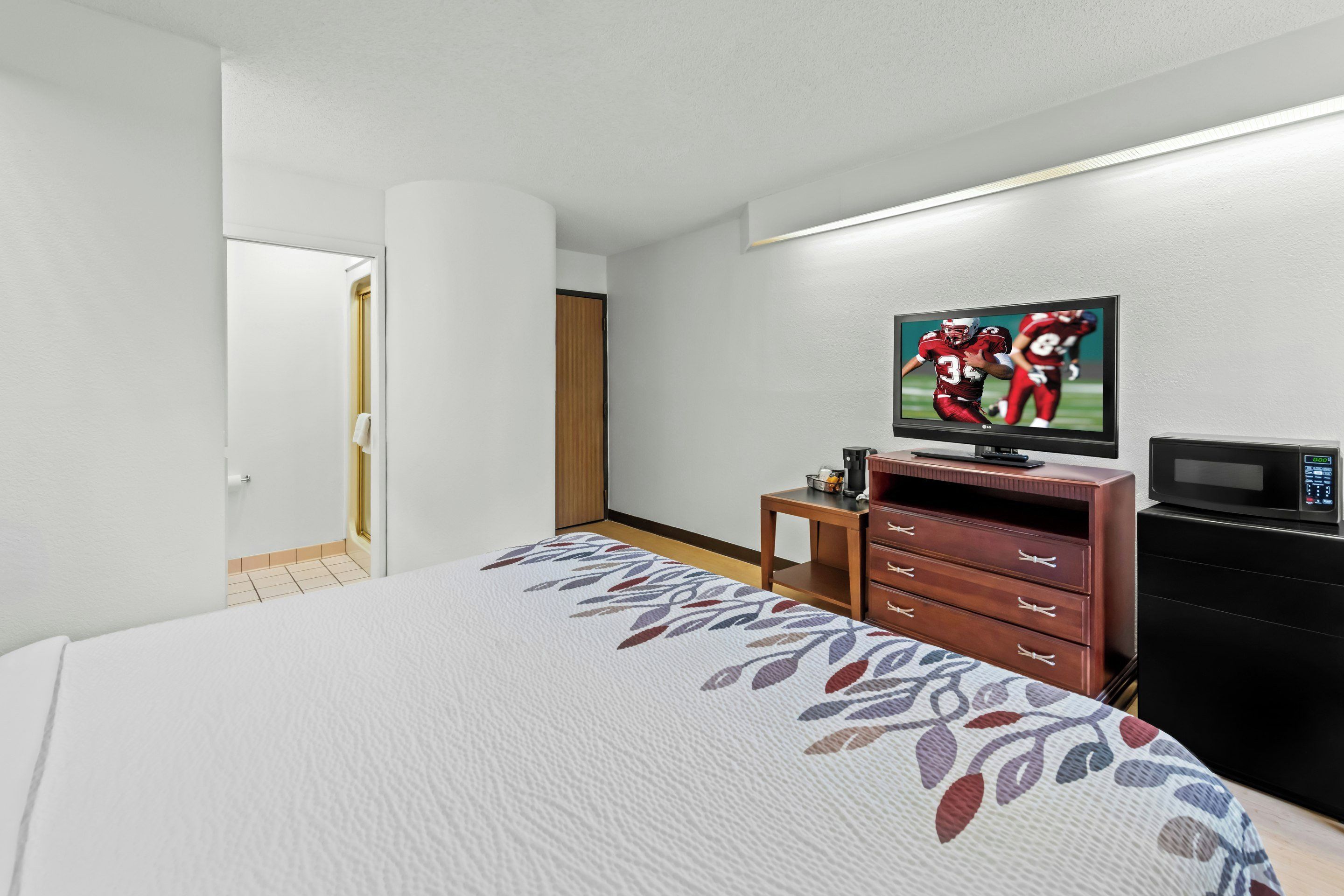 Una habitación de hotel con cama, televisión, microondas y cómoda de madera.