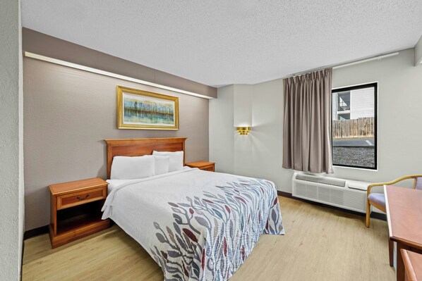 Habitación de hotel con cama, mesita de noche, lámpara, ventana y vista al exterior.