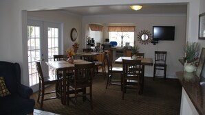 A dining area with a table and chairs, a kitchen in the background, and a television mounted on the wall. - National 9 - Nephi 9 Inn (Nephi)