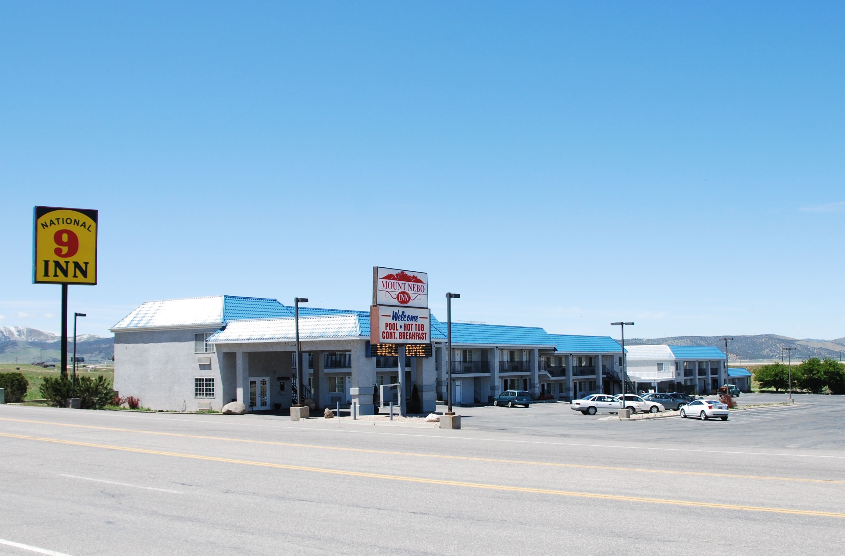 A motel with a blue roof and a signboard advertising amenities like a pool, hot tub, and breakfast.