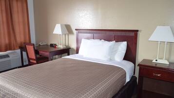A hotel room with a large bed, a desk with a chair, two bedside lamps, and a telephone.