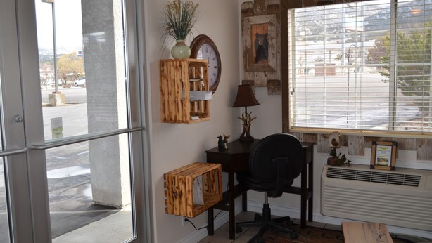 A room with a desk, chair, and window with blinds. There is a clock and a vase on the wall. - National 9 - Nephi 9 Inn (Nephi)