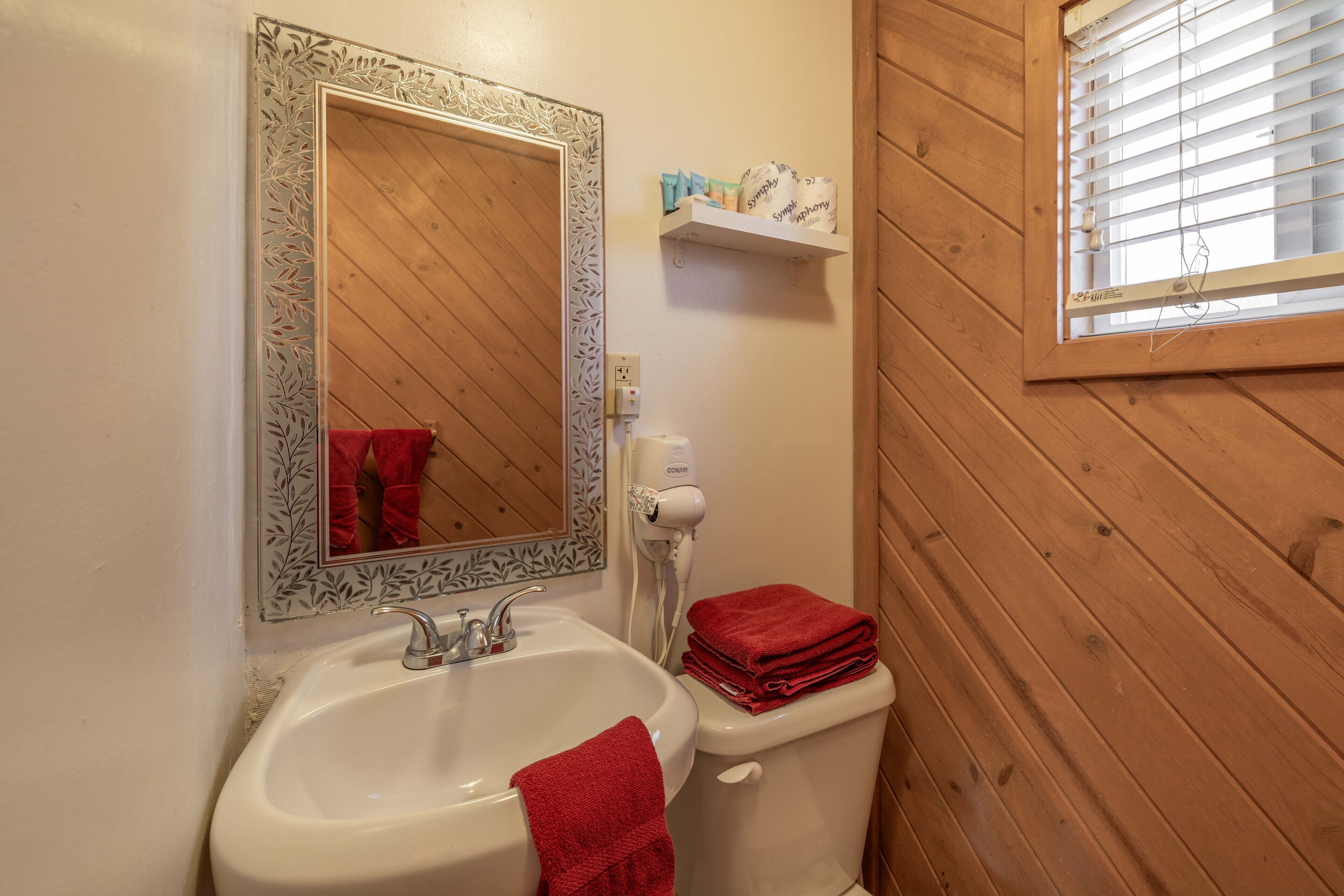 A bathroom with a white sink, a mirror with a decorative frame, a toilet, and a window with blinds.