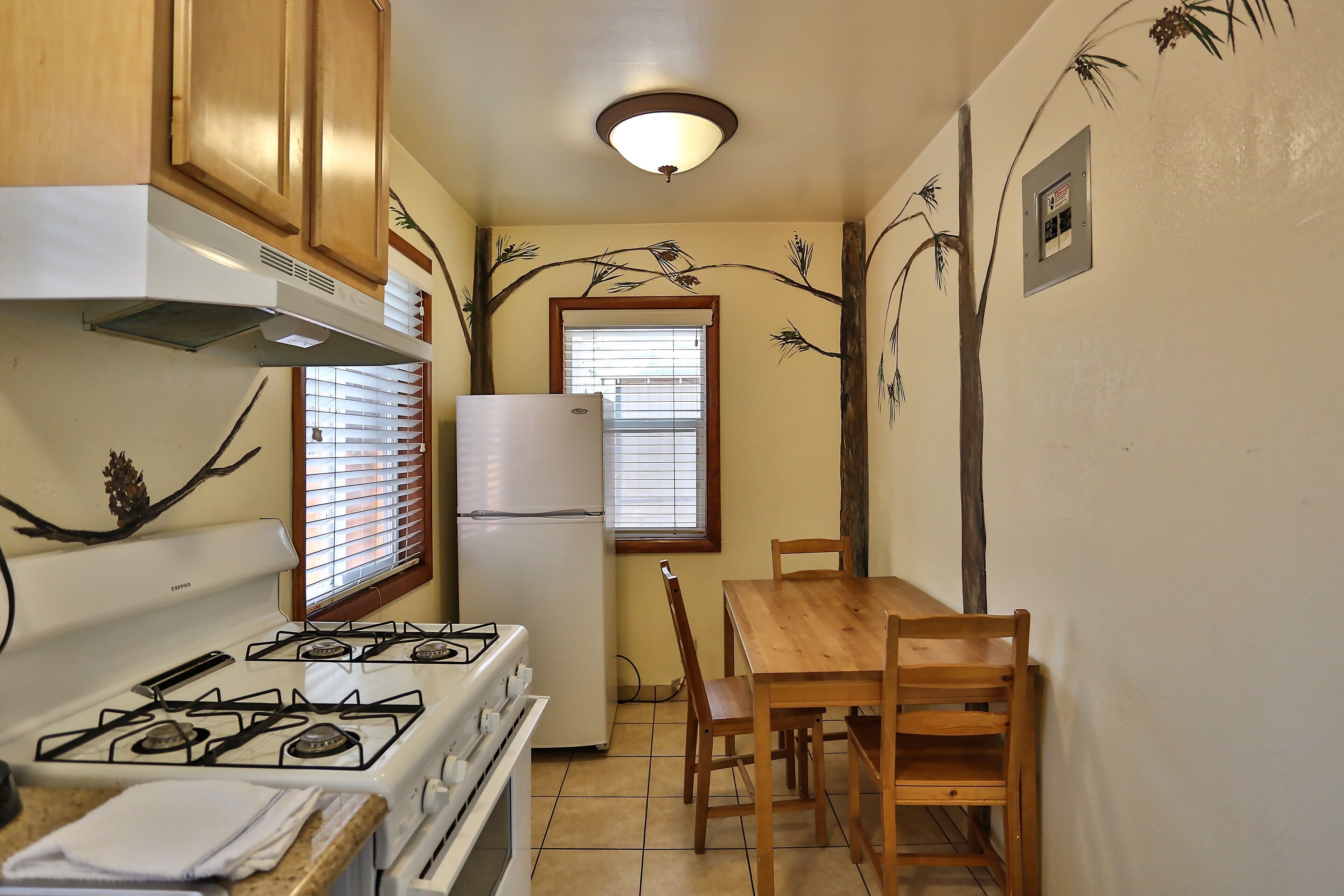 Una cocina con estufa, refrigerador y mesa de comedor de madera con sillas.