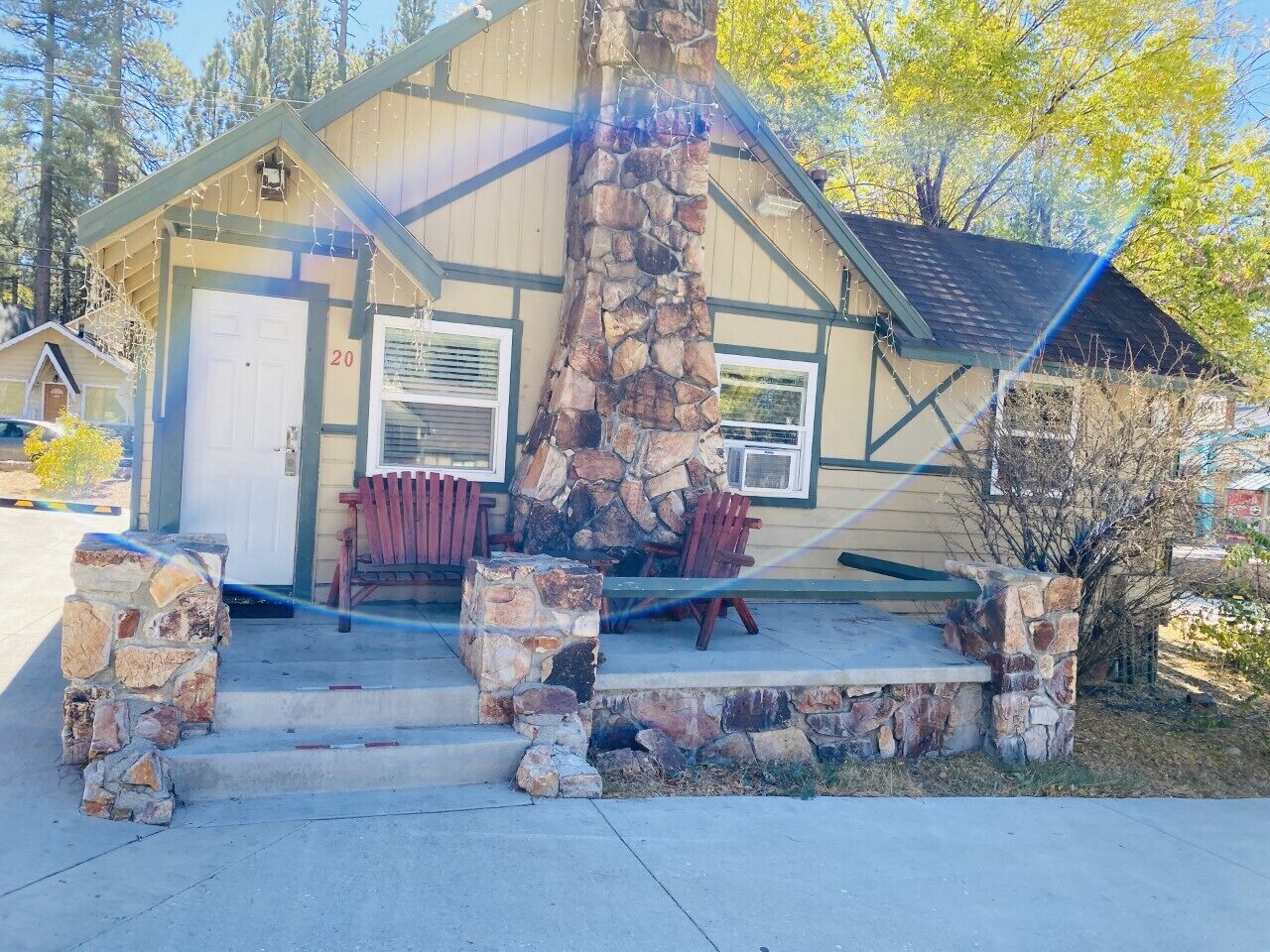 A rustic cabin with a stone chimney, a porch with red chairs, and a number '20' on the door.