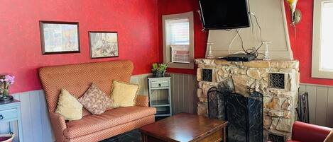 A living room with a red wall, a stone fireplace, a sofa, a coffee table, and a television mounted on the wall.
