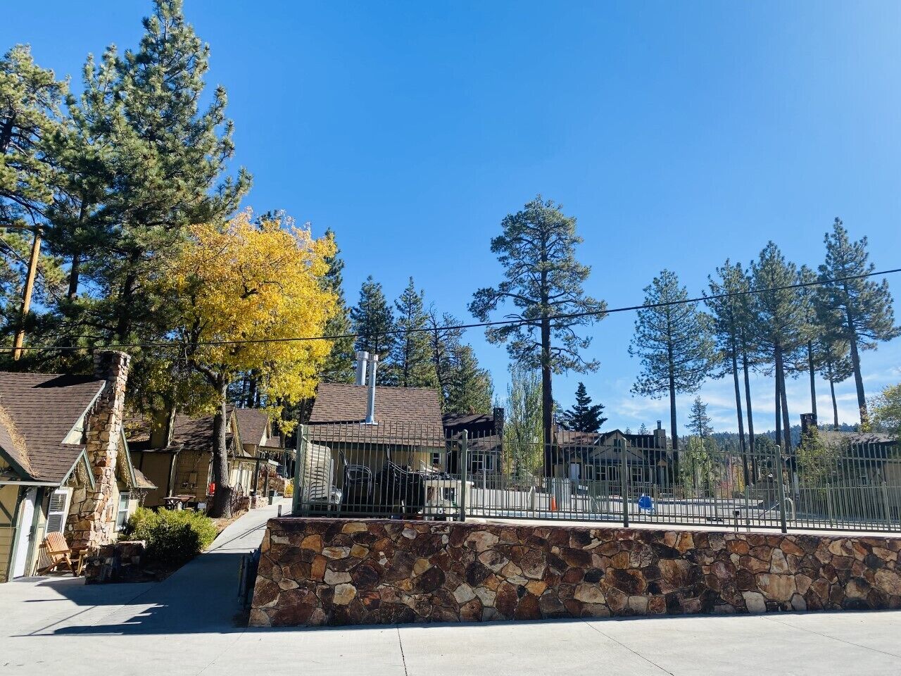 A residential area with stone walls, houses with sloped roofs, and tall trees.