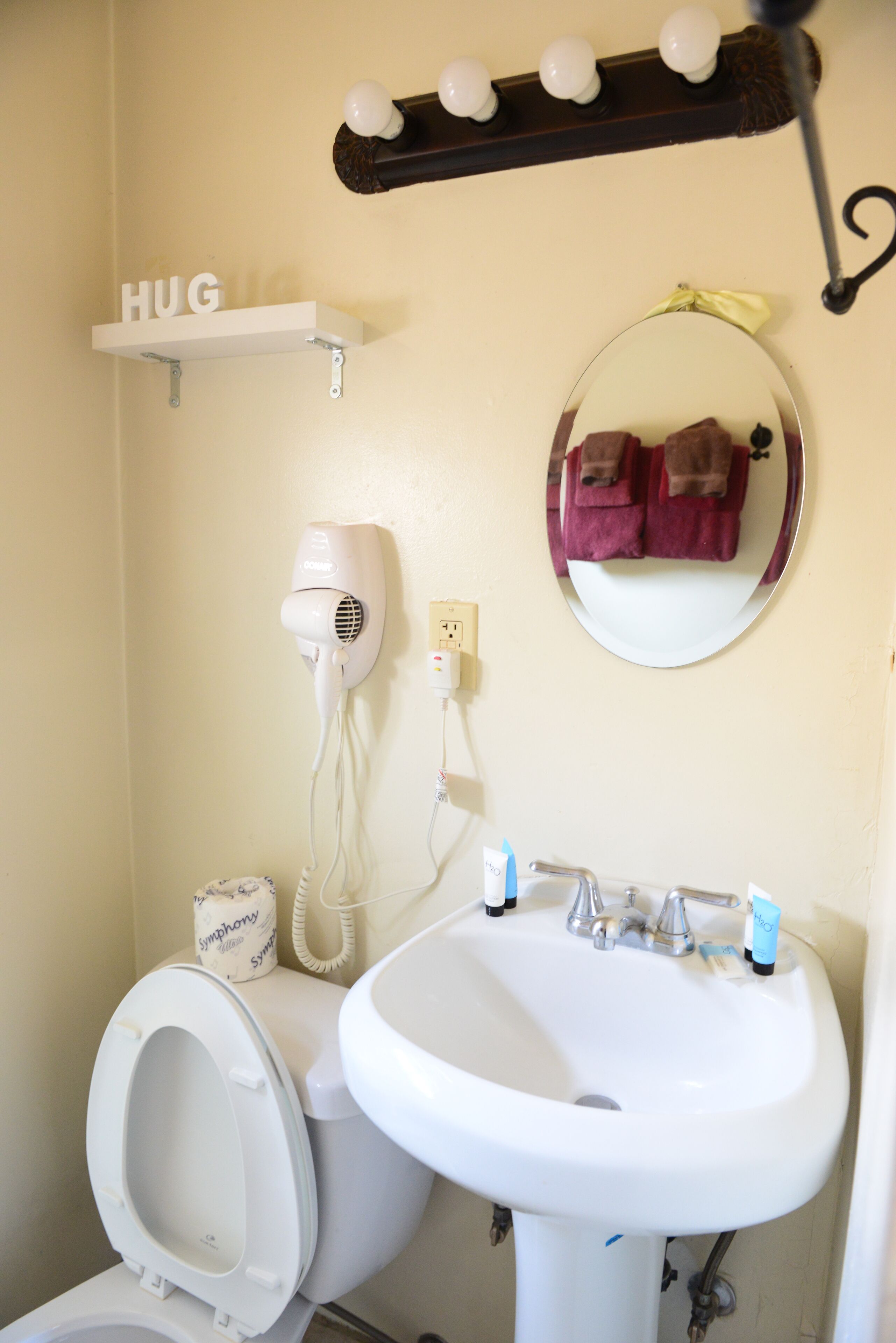 A bathroom with a white sink, a toilet, a hairdryer, a mirror, and a shelf with a 'HUG' sign.