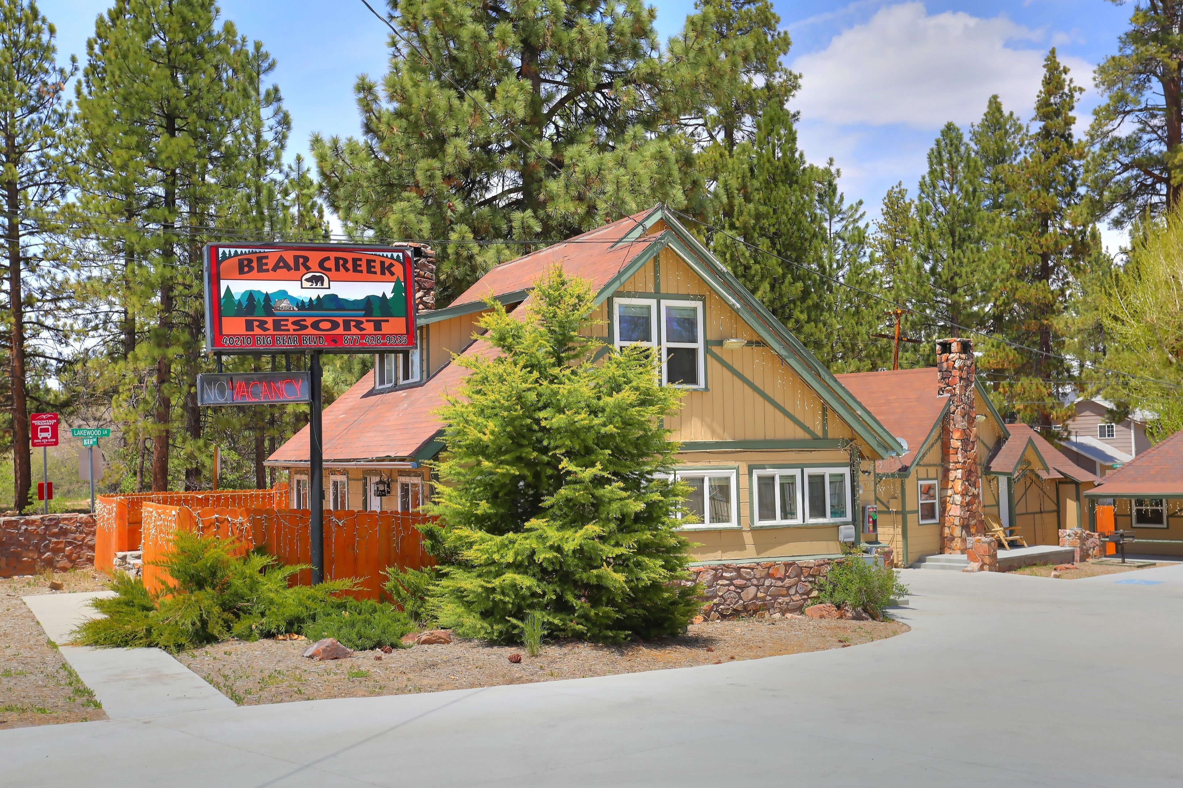 A two-story building with a stone chimney, a large evergreen tree in front, and a sign for Bear Creek Resort.