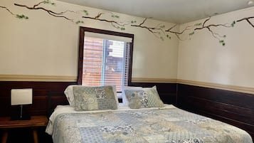Un dormitorio con una cama grande, dos almohadas, una mesita de noche y una ventana con persianas.