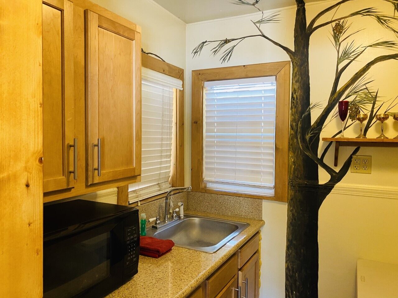 Una cocina con armarios de madera, un microondas negro, un fregadero y un árbol decorativo.