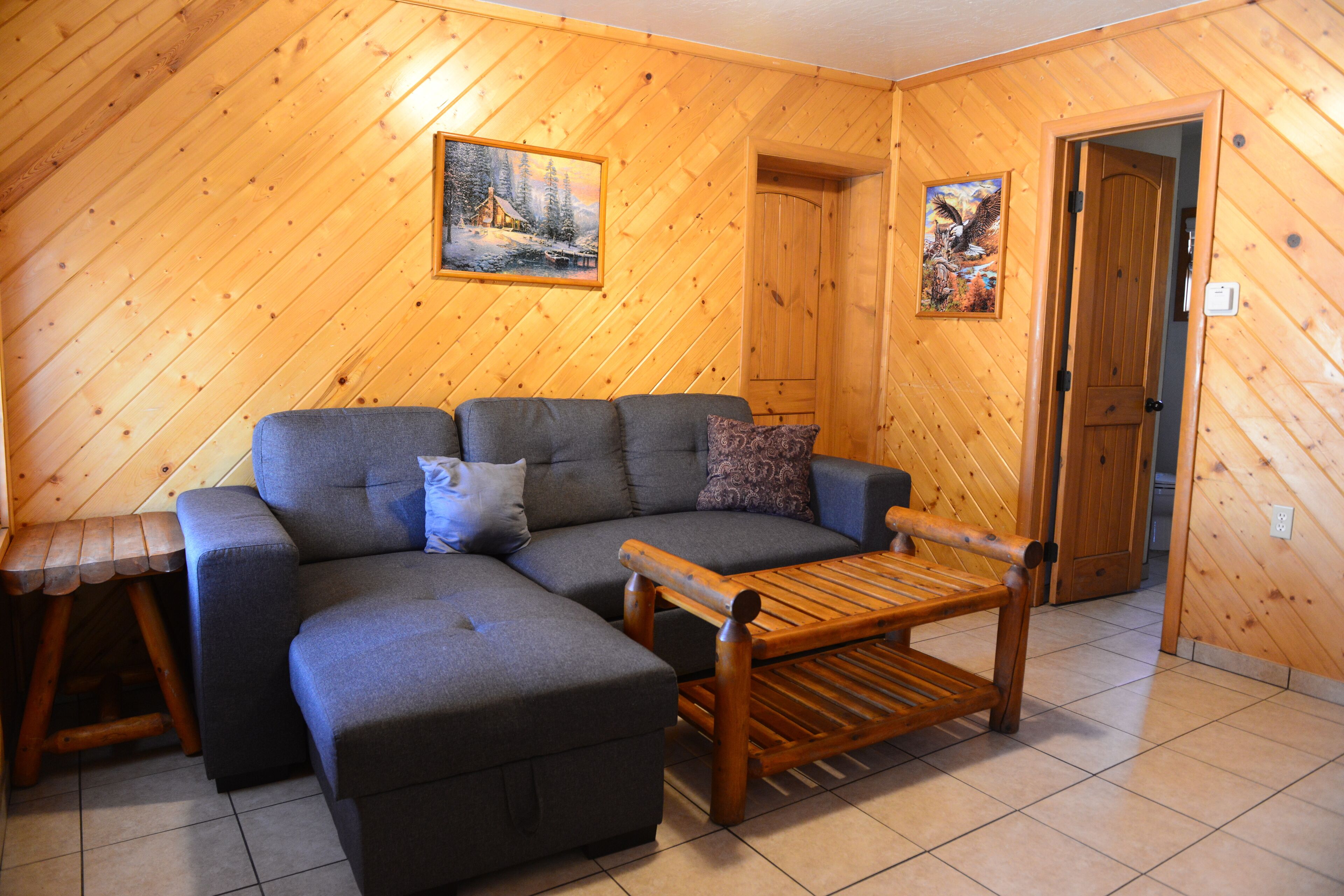 A wooden-paneled room with a grey sectional sofa, a wooden bench, and a small table.