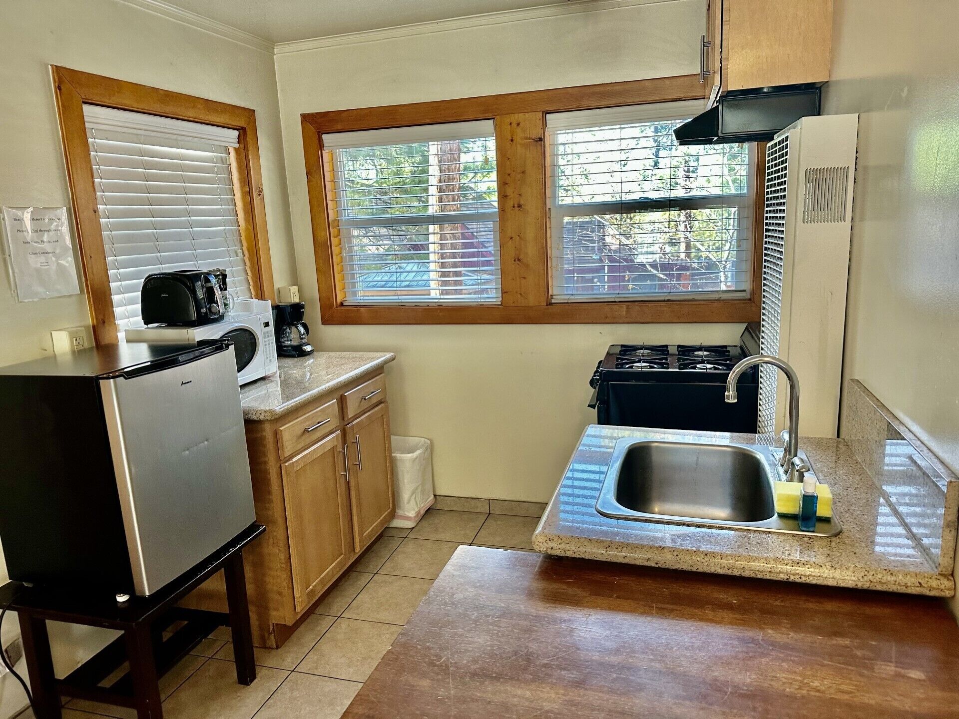 A compact kitchen with a refrigerator, microwave, stove, sink, and wooden cabinets.