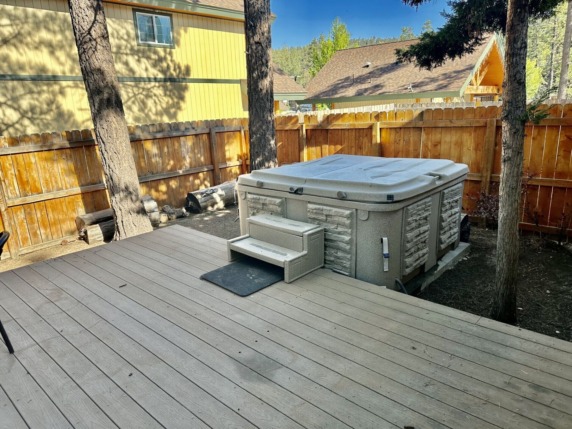 A hot tub on a wooden deck with a wooden fence and trees in the background.